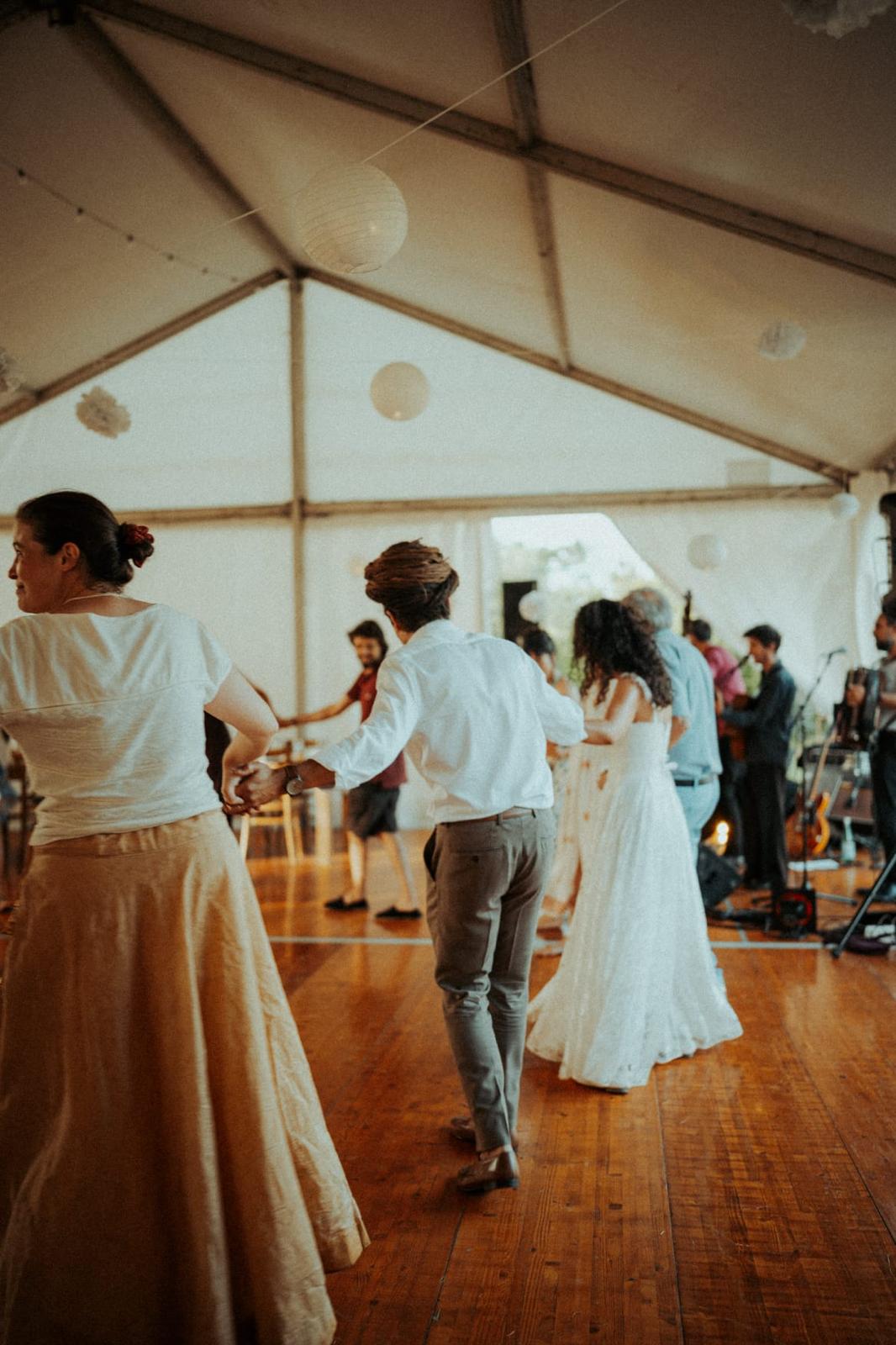 Des gens dansent joyeusement sur un parquet en bois sous une tente décorée de lanternes, avec un groupe de musique en arrière-plan.