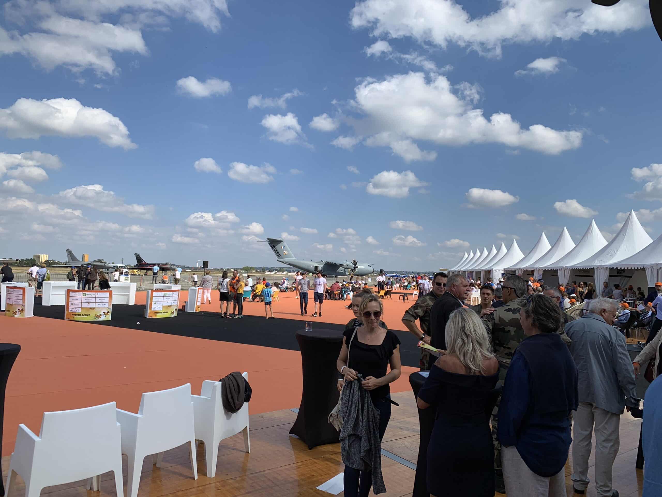 Foule lors d'un meeting aérien, grands avions militaires dont un Airbus A400M, tentes blanches et ciel bleu nuageux.