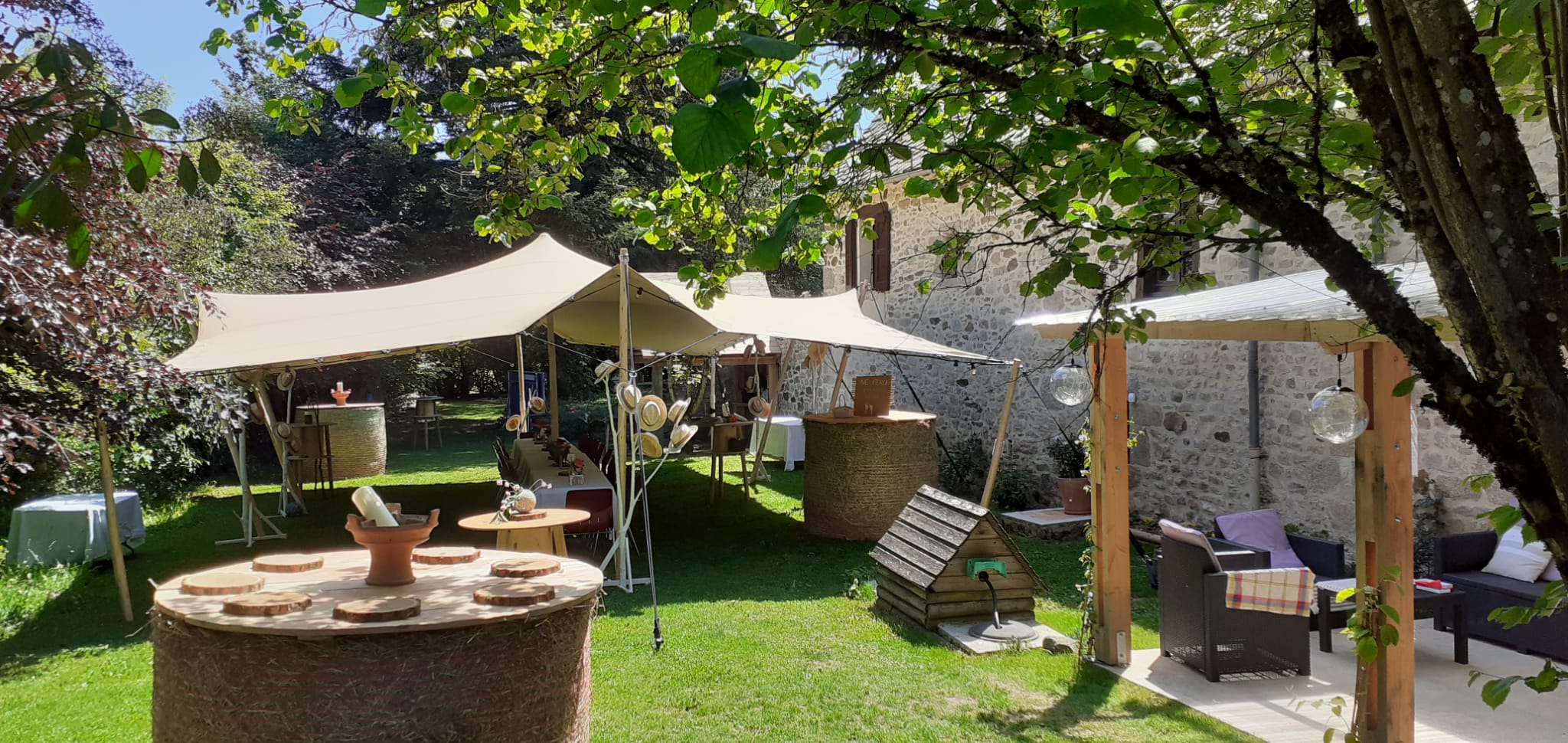 Réception de mariage champêtre avec tente stretch et tables en foin dans le jardin d'une maison en pierre.