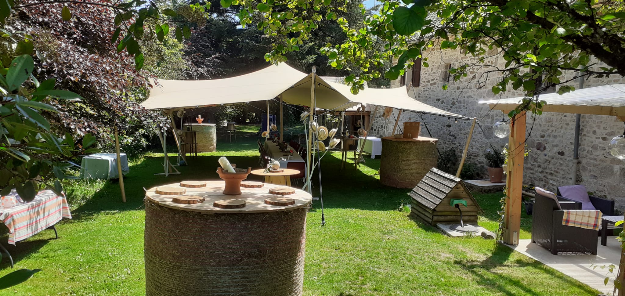 Réception champêtre avec tente nomade, tables en bottes de paille et jardin fleuri devant une bâtisse en pierre.