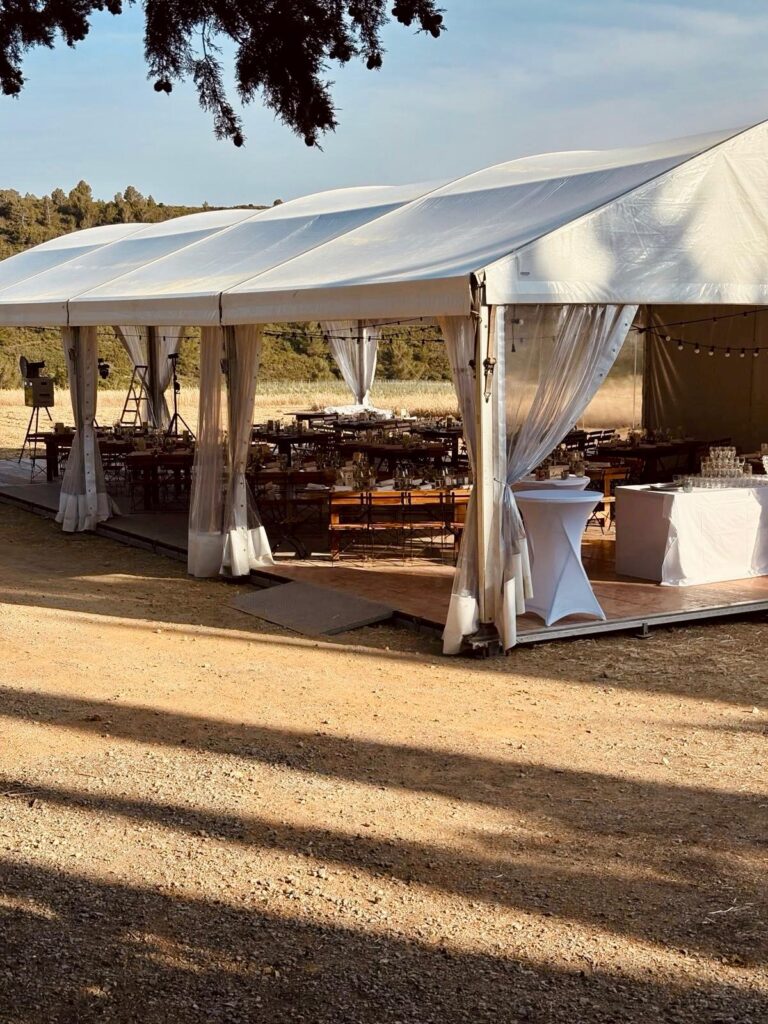 Grande tente blanche de réception installée en extérieur sur plancher, avec tables dressées pour un événement, sous un ciel dégagé.