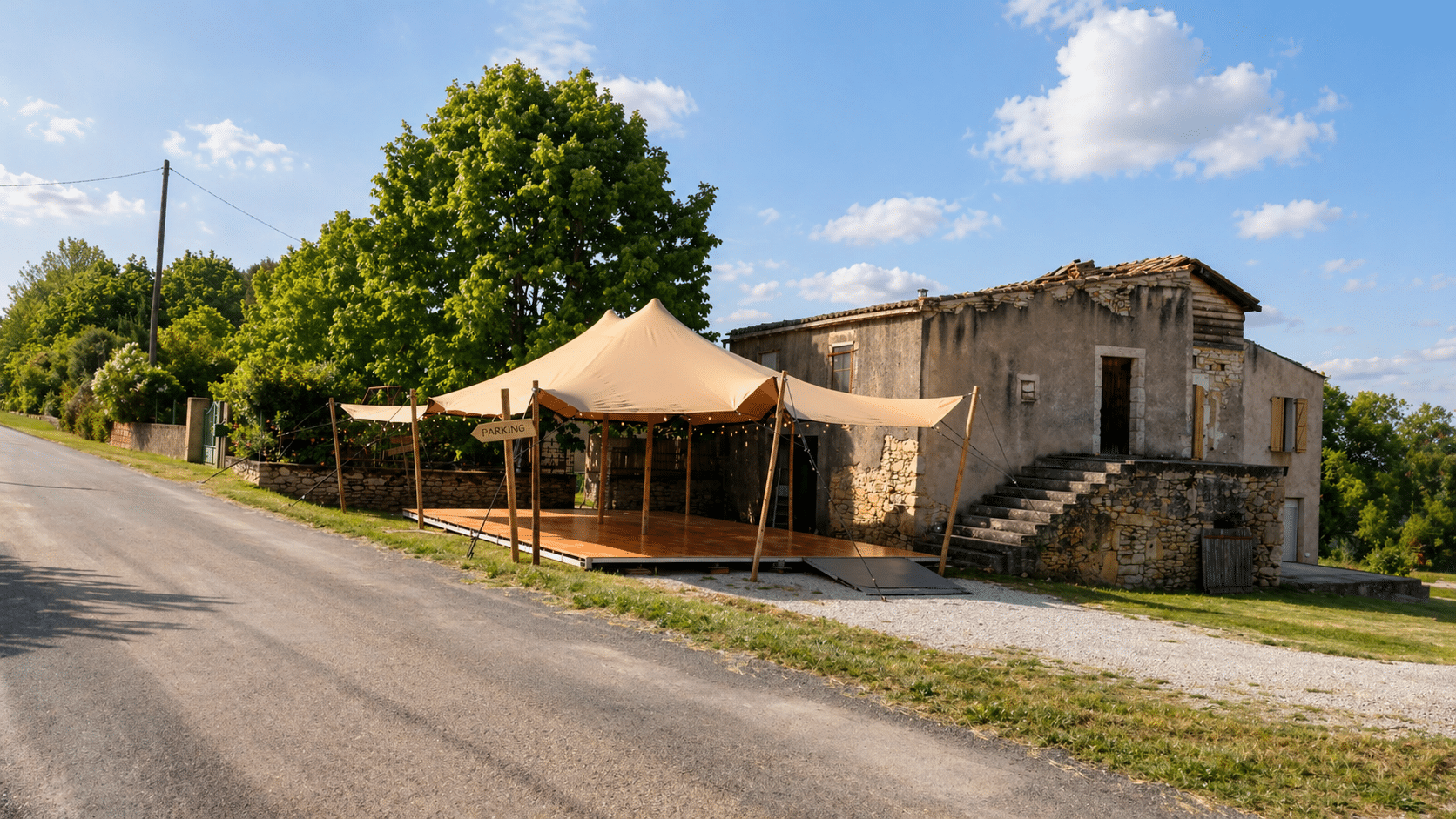 Grande tente nomade beige avec panneau parking et terrasse bois devant une vieille maison en pierre.