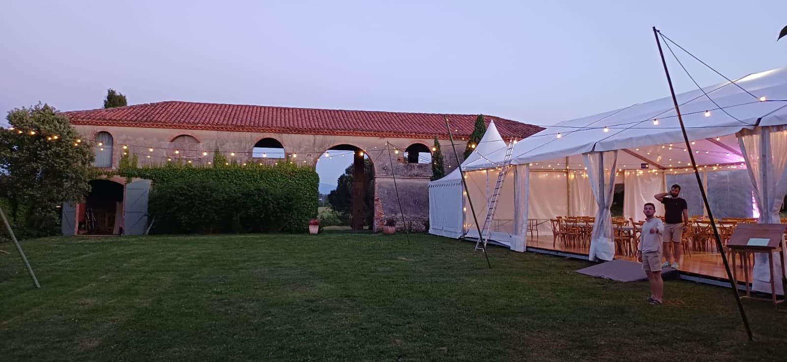 Chapiteau de réception illuminé près d'une bâtisse ancienne en pierre au crépuscule pour un événement élégant.