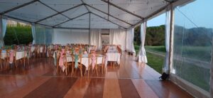 Intérieur d'un chapiteau de réception avec tables dressées et chaises décorées sur un plancher en bois élégant.