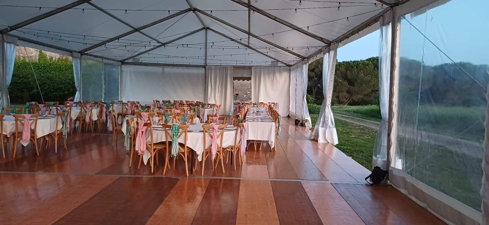 Intérieur d'un chapiteau de réception avec tables dressées et chaises décorées sur un plancher en bois élégant.