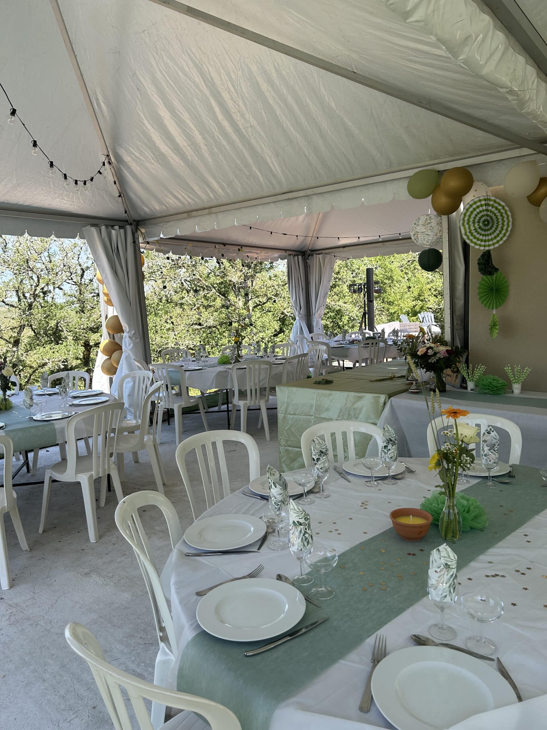 Décoration de réception sous chapiteau avec tables blanches, chemins de table vert sauge et ballons dorés.