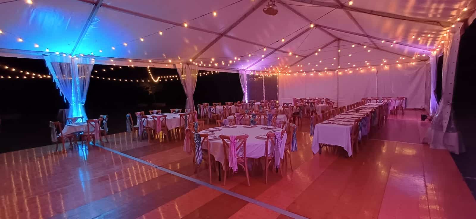 Tente événementielle décorée de guirlandes, piste de danse et tables élégantes sous un éclairage festif rose et bleu.