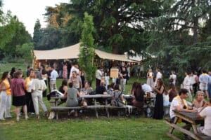 Réception en plein air sous une tente stretch avec des invités en tenue élégante discutant dans un jardin arboré.