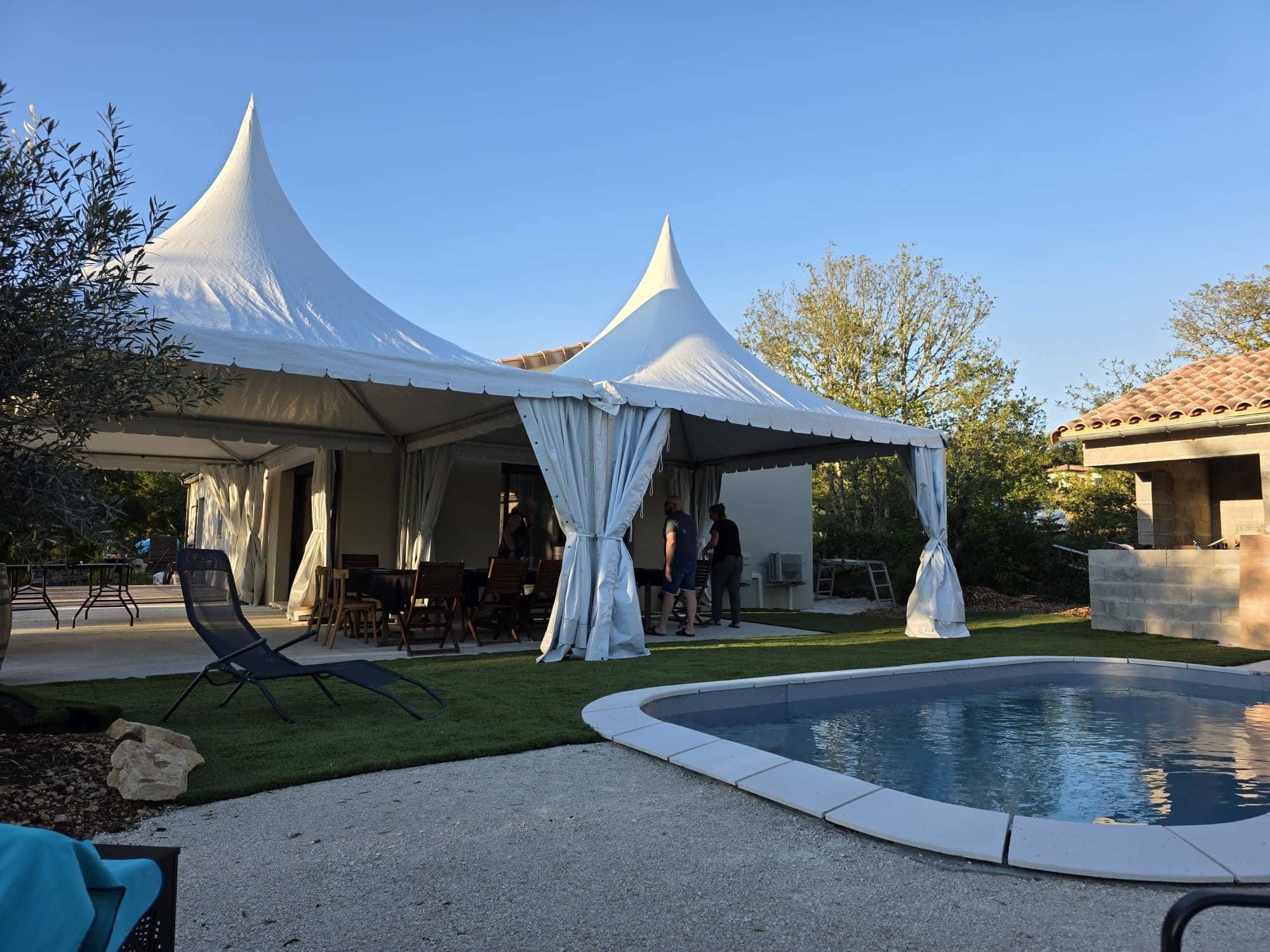 Chapiteaux blancs de réception installés au bord d'une piscine pour un événement extérieur ensoleillé.