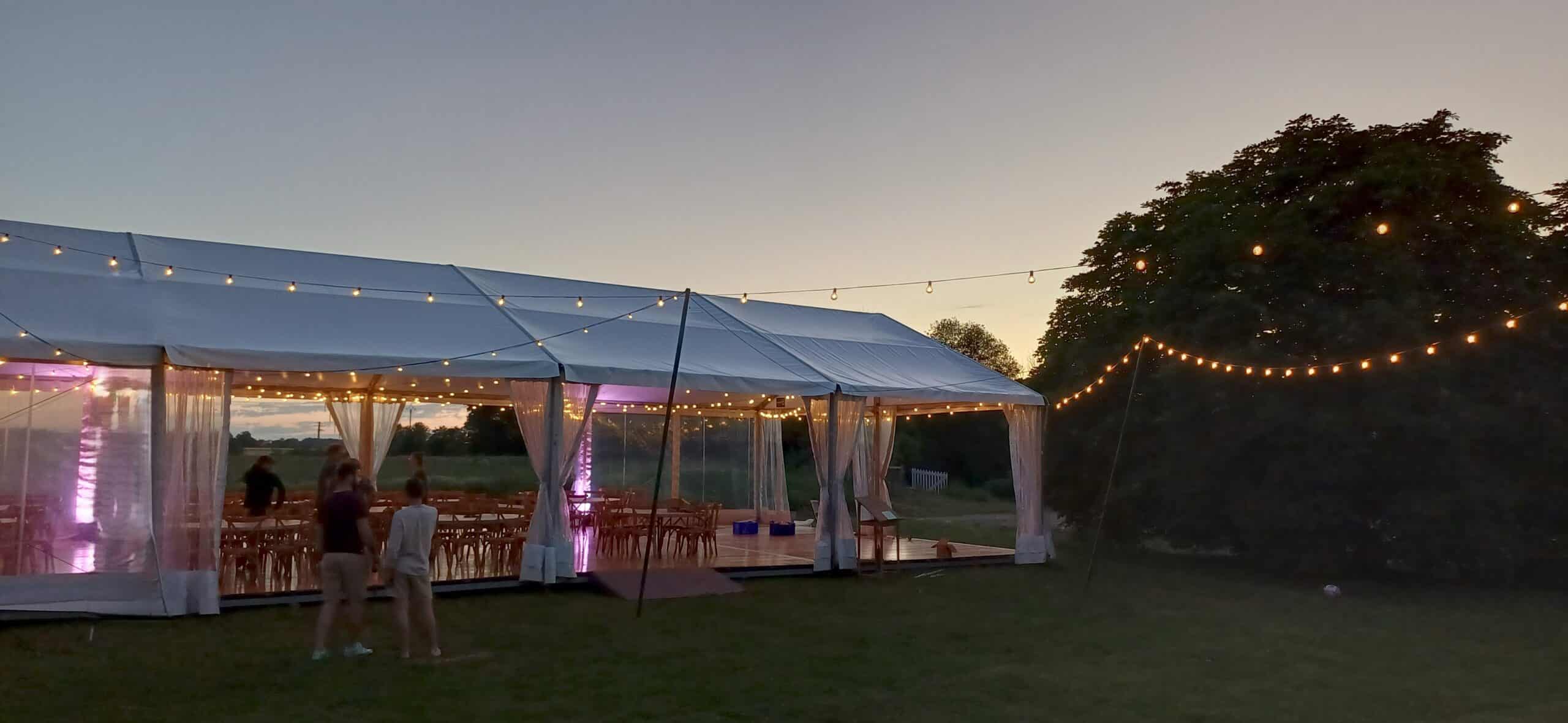 Grande tente de réception blanche illuminée par des guirlandes guinguettes au crépuscule pour un événement festif.