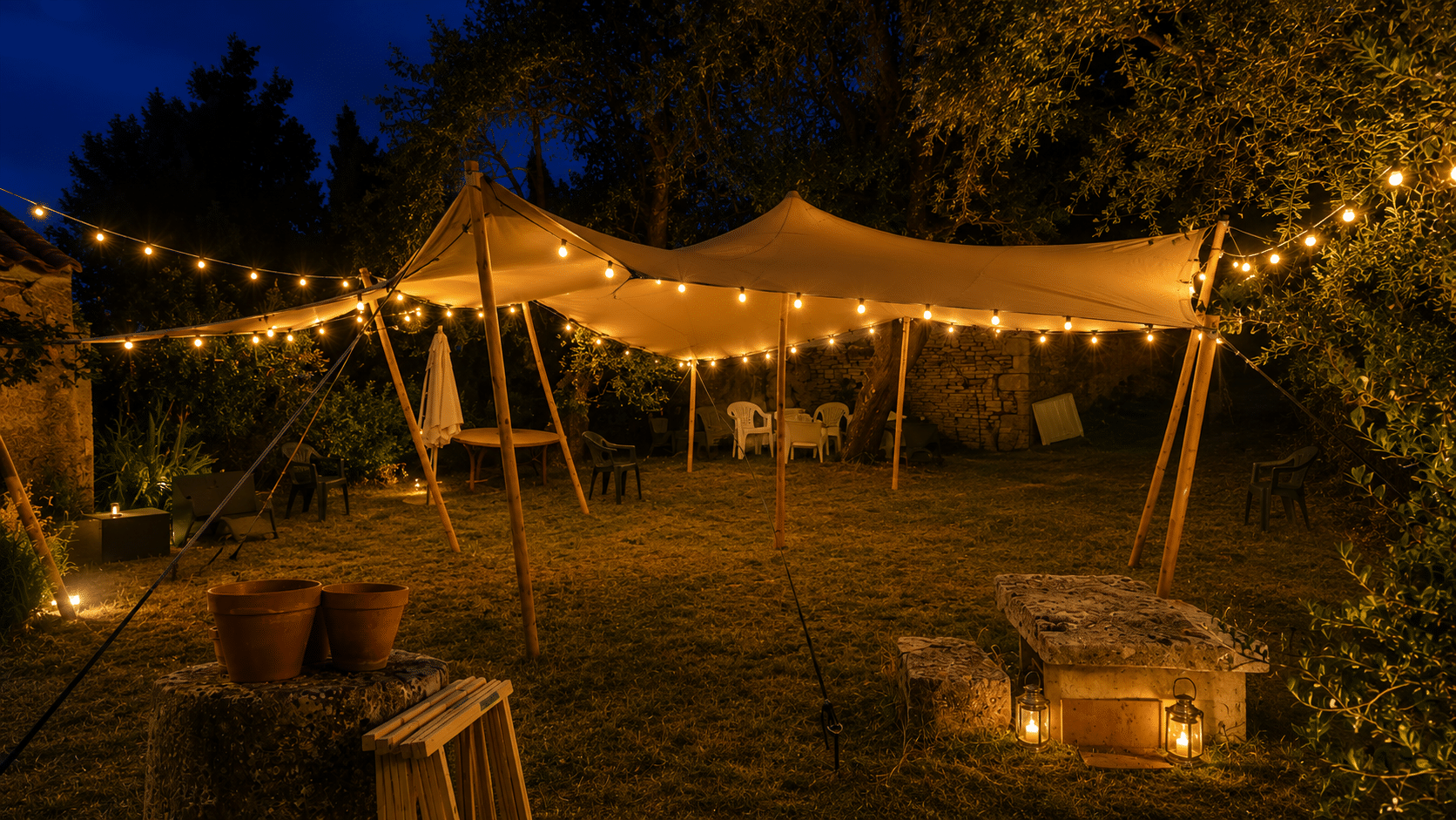 Tente stretch illuminée de guirlandes dans un jardin de nuit avec lanternes et mobilier de réception.