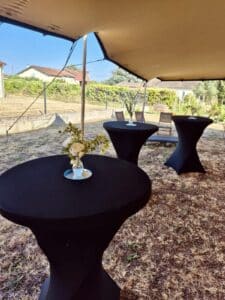 Tables hautes noires avec fleurs sous une tente de réception en plein air pour un événement.