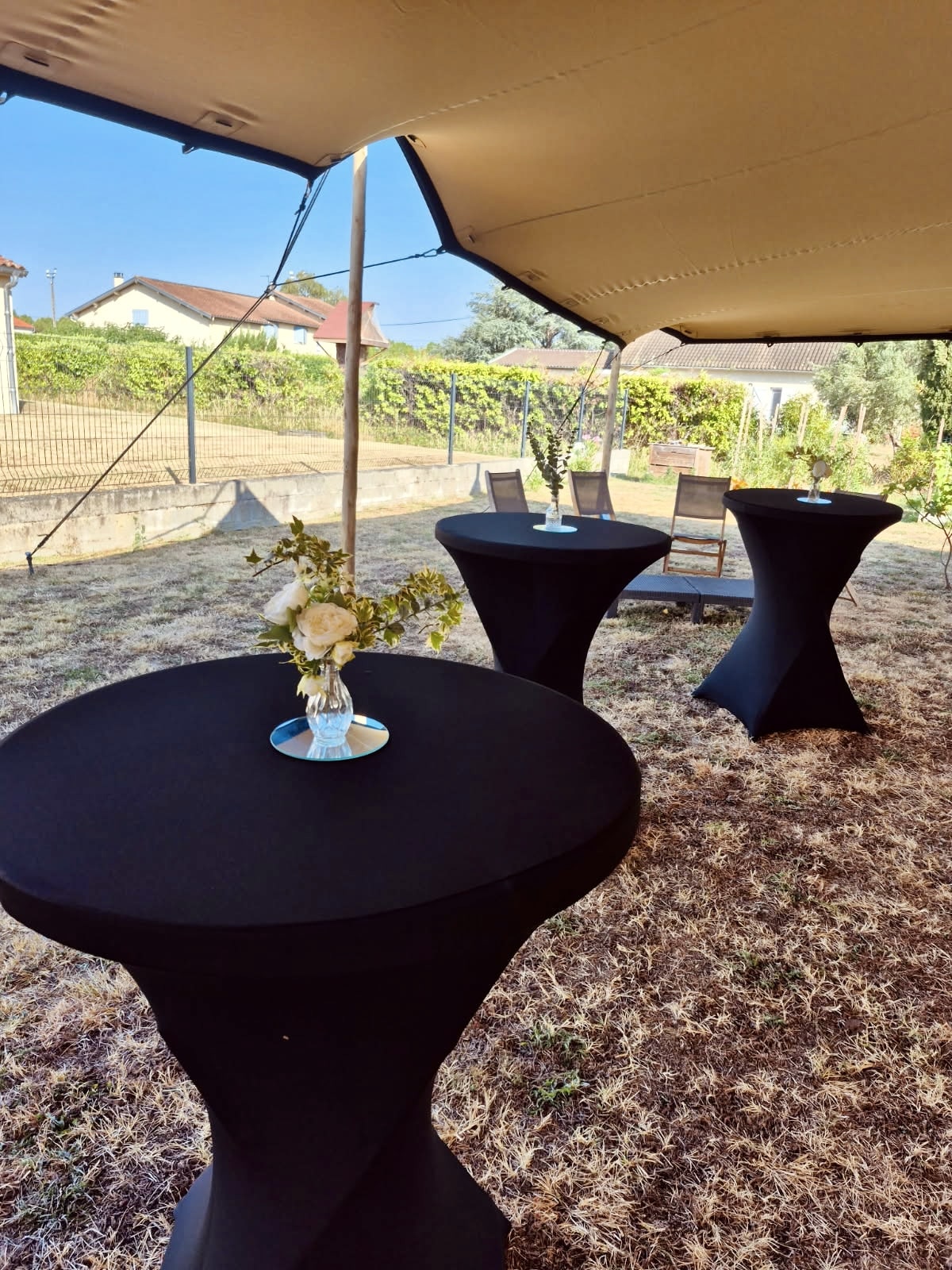 Tables hautes noires avec fleurs sous une tente de réception en plein air pour un événement.