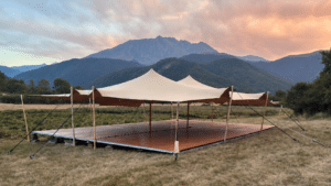 Chapiteau stretch beige et plancher bois face aux montagnes au crépuscule.