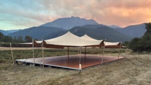 Tente nomade beige sur plancher bois face aux montagnes au coucher du soleil.