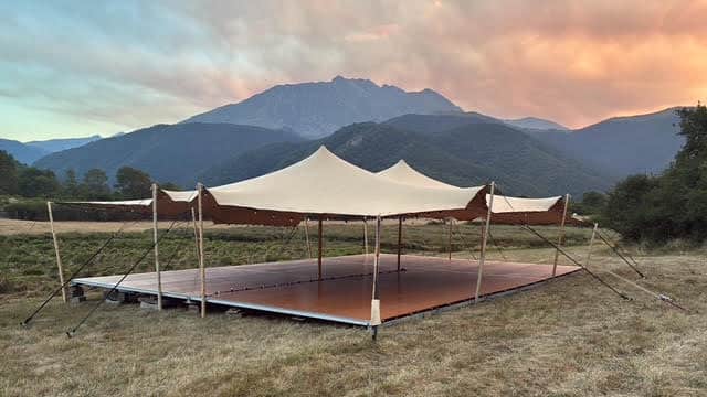 Tente nomade beige sur plancher bois face aux montagnes au coucher du soleil.