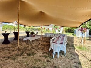 Tente stretch beige, tables de réception dressées et mange-debout noirs pour un événement extérieur convivial.