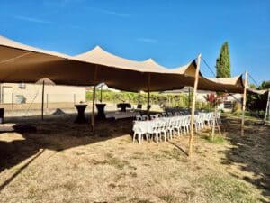 Tente nomade beige, tables et chaises blanches pour réception en plein air dans un jardin ensoleillé.