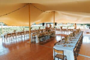Réception sous tente stretch beige avec tables dressées et guirlandes sur parquet.