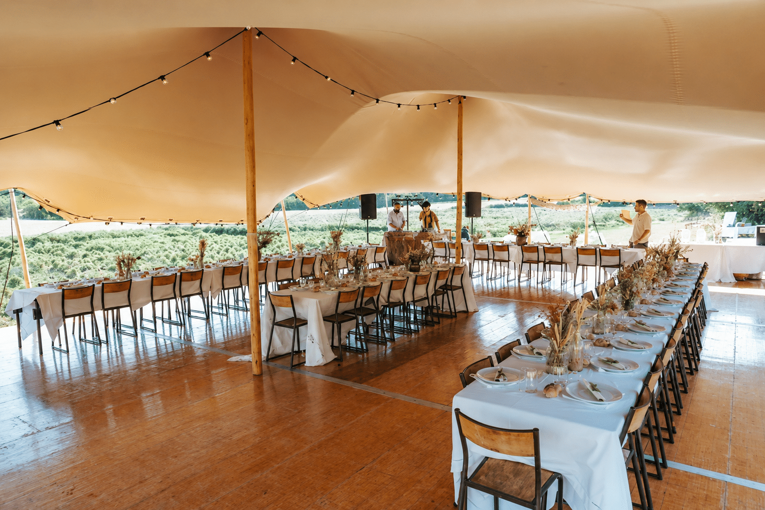 Réception sous une grande tente nomade beige avec tables dressées et plancher en bois dans un cadre champêtre.