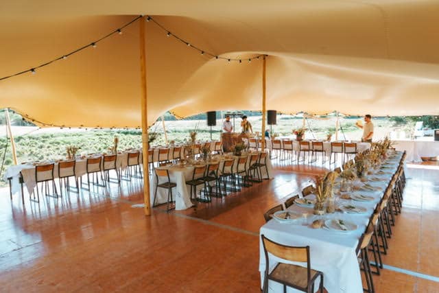 Réception sous tente stretch beige avec tables dressées et guirlandes sur parquet.