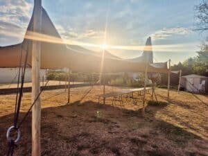 Tente nomade stretch beige et tables pliantes dans un jardin au coucher du soleil.