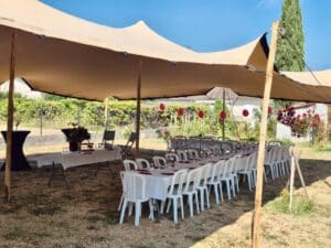 Tente stretch nomade beige, tables de réception nappées et ballons rouges dans un jardin ensoleillé pour un événement.