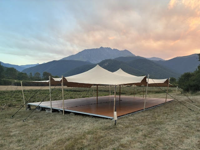 Chapiteau stretch beige sur plancher bois devant des montagnes au coucher du soleil.