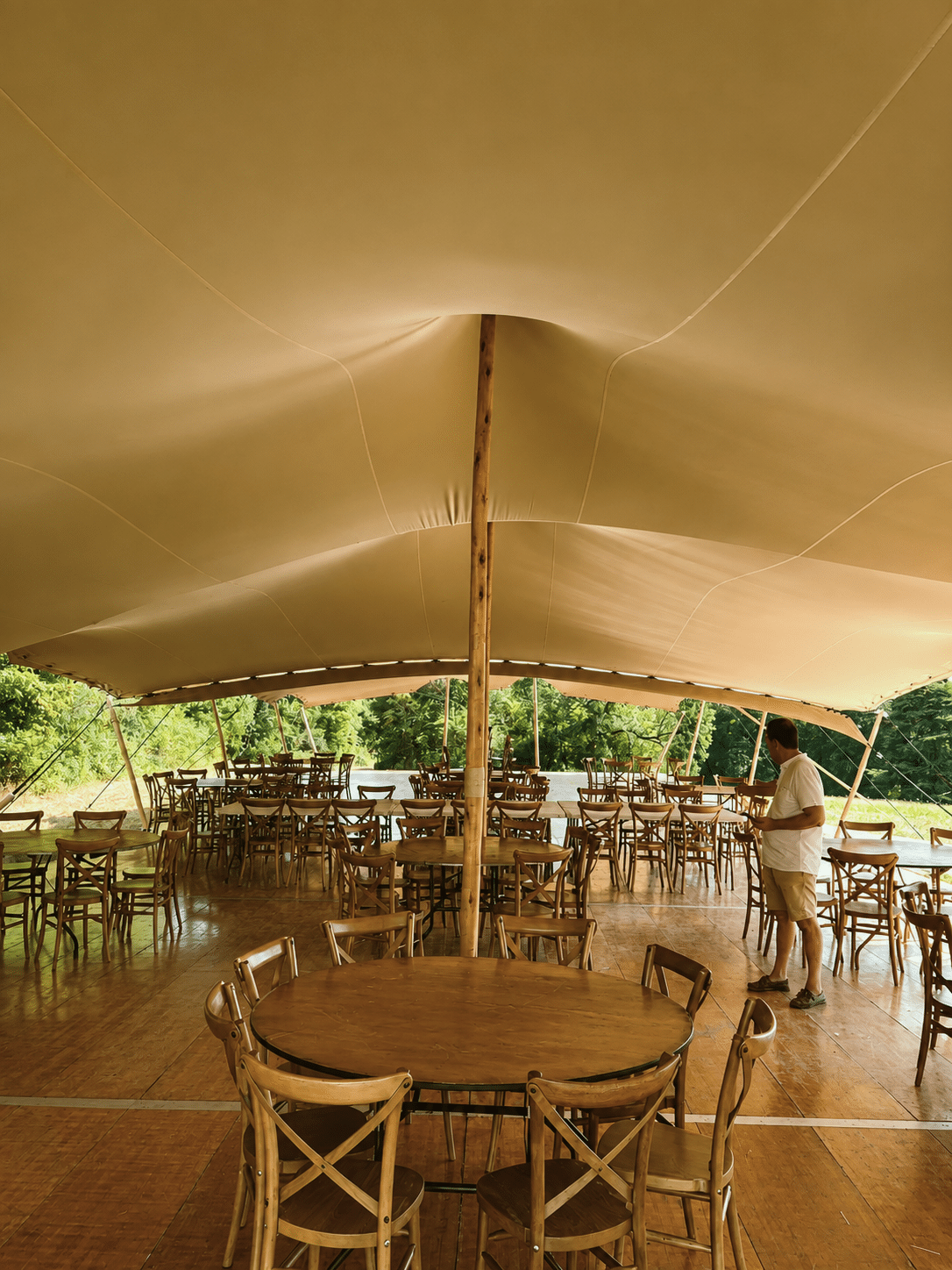 Chapiteau nomade beige avec tables rondes en bois et chaises crossback sur plancher pour réception événementielle.