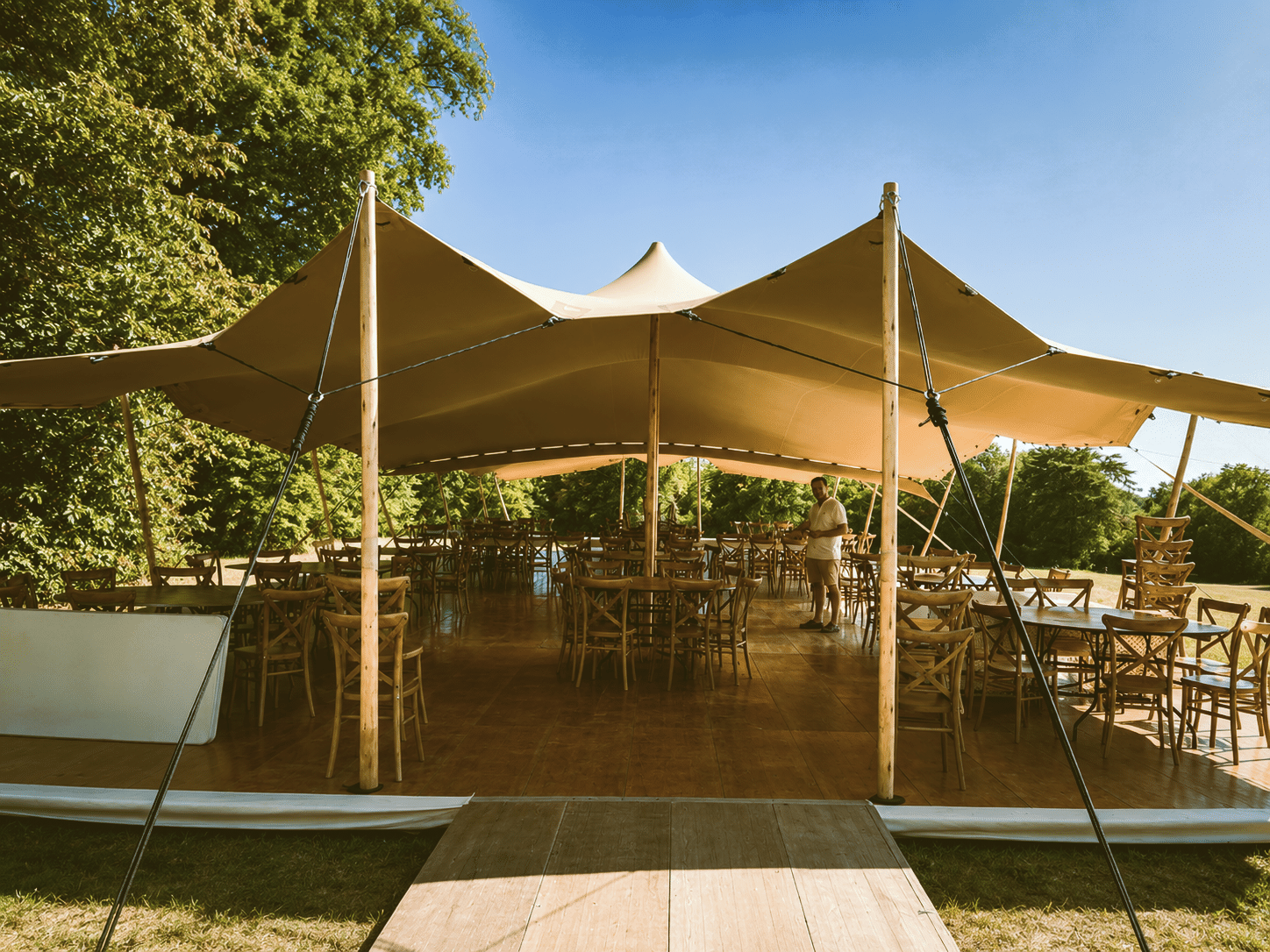 Tente nomade beige avec parquet et chaises en bois pour réception champêtre en plein air.