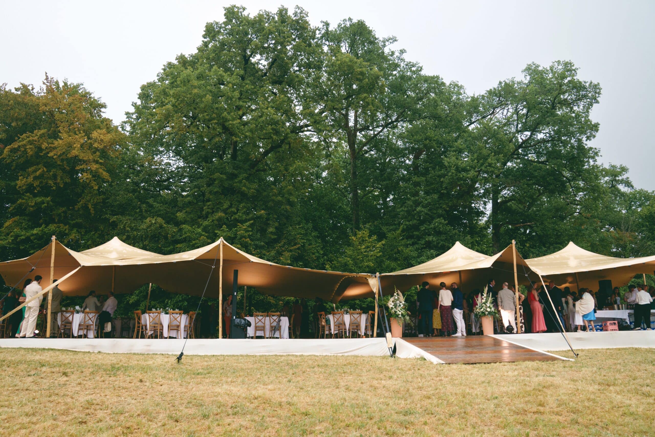 Tente nomade beige pour réception de mariage en extérieur avec invités devant une forêt.